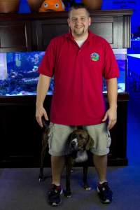 Jon standing in front of an aquarium with a dog between his legs